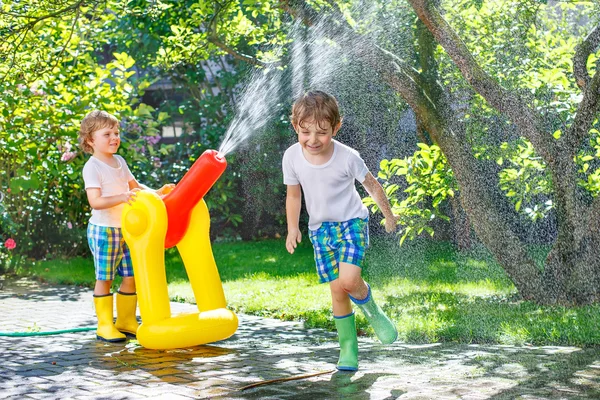 Zwei kleine Kinder spielen im Sommer mit Gartenschlauch und Wasser — Stockfoto