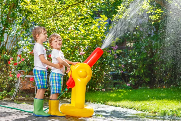 Zwei kleine Kinder spielen im Sommer mit Gartenschlauch und Wasser — Stockfoto