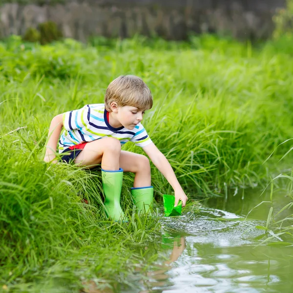 Cute little boy playing with paper boats by a river — Stock Photo, Image