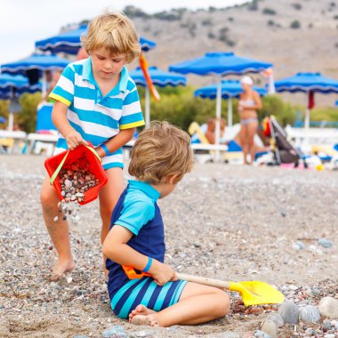 Two little kid boys playing on beach with stones