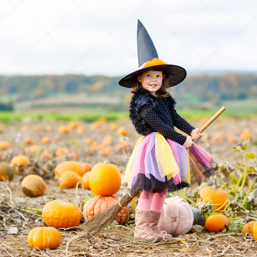 little girl wearing halloween witch costume on pumpkin patch