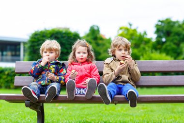 drie broers en zussen zittend op een bankje en het eten van chocolade.