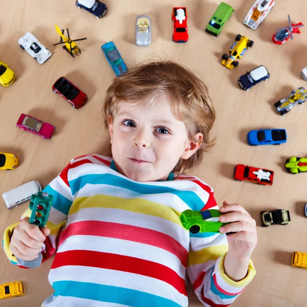 Pequena criança loira brincando com muitos carros de brinquedo interior — Fotografia de Stock