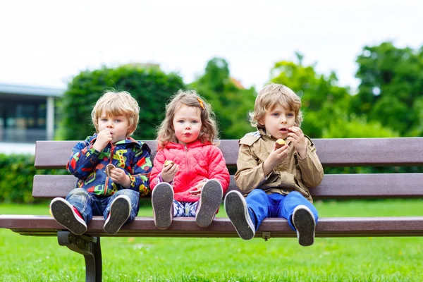 Drie broers en zussen zittend op een bankje en het eten van chocolade. — Stockfoto