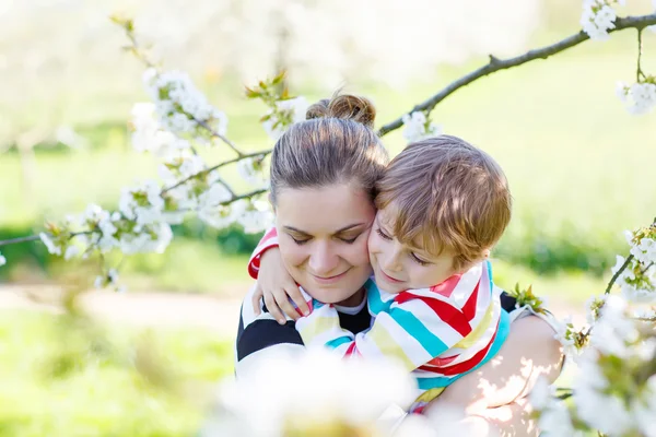 Ung mamma och lilla kid boy roar sig i blommande trädgård — Stockfoto