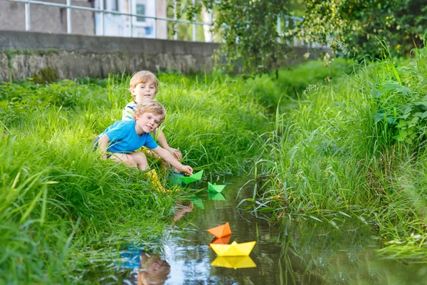 Two little brothers playing with paper boats by a river — Stock Photo, Image