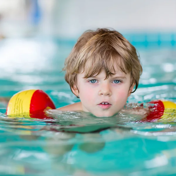 Mały chłopiec dziecko z swimmies uczyć się pływać w krytym basenem — Zdjęcie stockowe