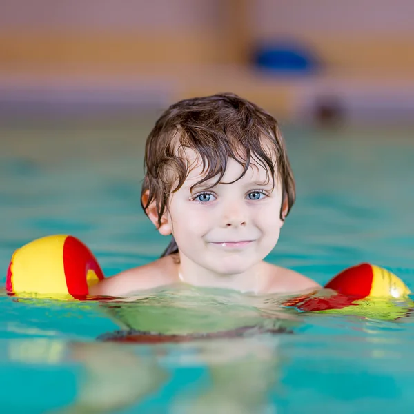 Mały chłopiec dziecko z swimmies uczyć się pływać w krytym basenem — Zdjęcie stockowe