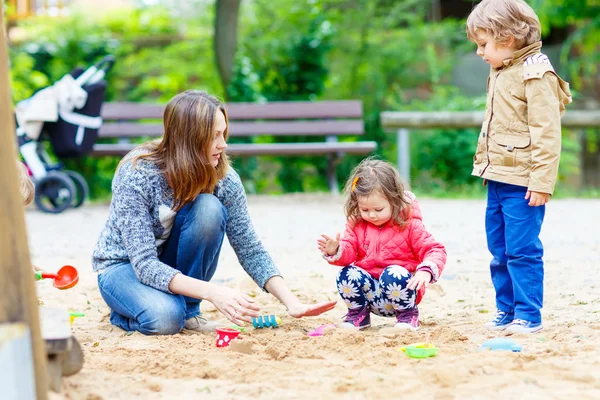 Madre y dos niños pequeños jugando en el patio de recreo —  Fotos de Stock