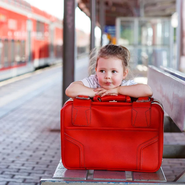 Niña con una gran maleta roja en una estación de tren — Foto de Stock