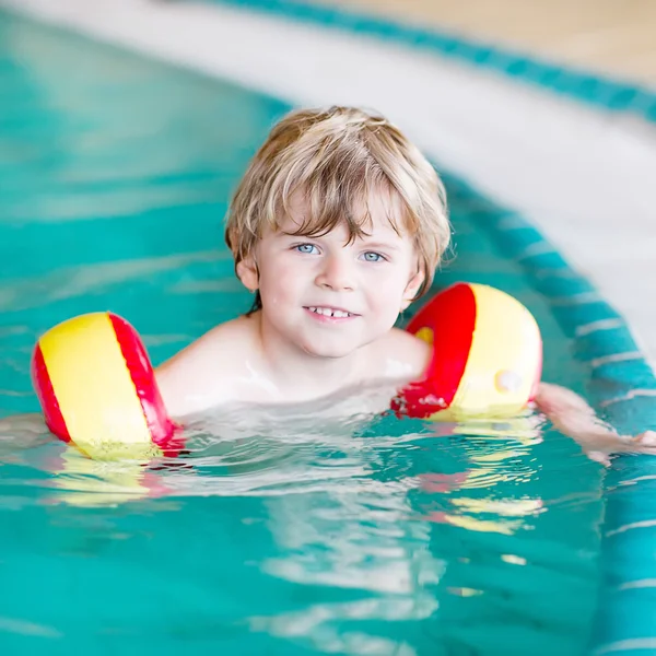 Mały chłopiec dziecko z swimmies uczyć się pływać w krytym basenem — Zdjęcie stockowe