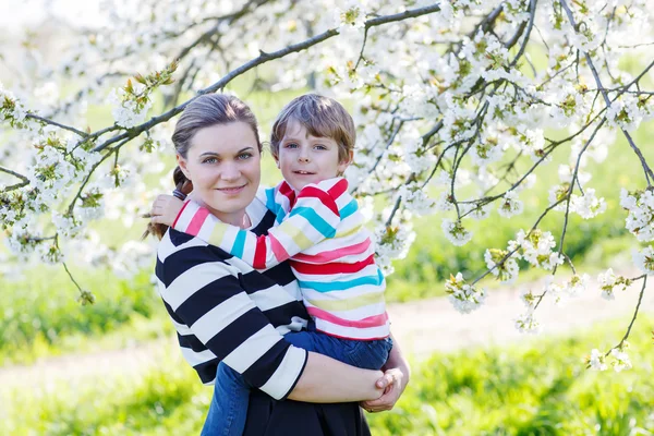 Mladá matka a dítě chlapec v rozkvetlé zahradě — Stock fotografie