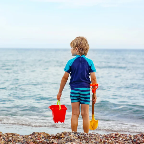 Little blond kid boy standing on lonely ocean beach — Stock fotografie