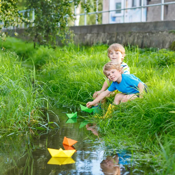 Two little brothers playing with paper boats by a river — Stock Photo, Image