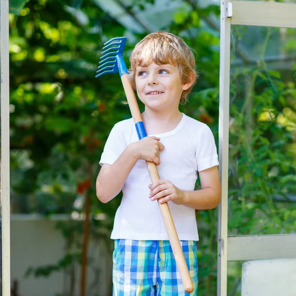 Menino pequeno que trabalha com enxada de jardim em estufa — Fotografia de Stock