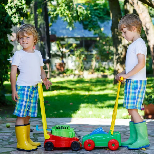 Two little boys playing with lawn mower toys — Stock Photo, Image