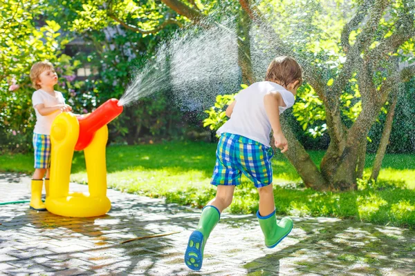 Due bambini piccoli che giocano con tubo da giardino e acqua in estate — Foto Stock