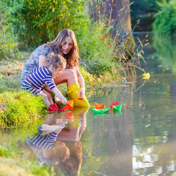 Adorável menina e sua mãe brincando com barcos de papel em um r — Fotografia de Stock