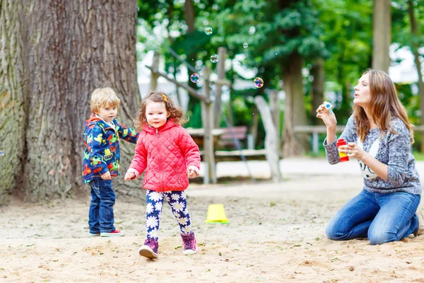 Moeder en twee kleine kinderen spelen op speelplaats — Stockfoto