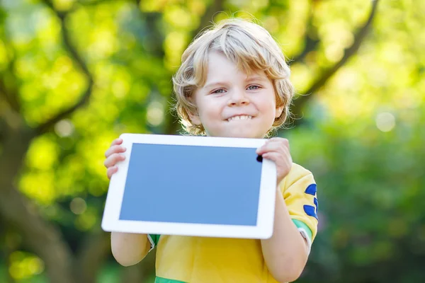 Счастливый маленький ребенок, держа в руках планшетный компьютер, на улице — стоковое фото