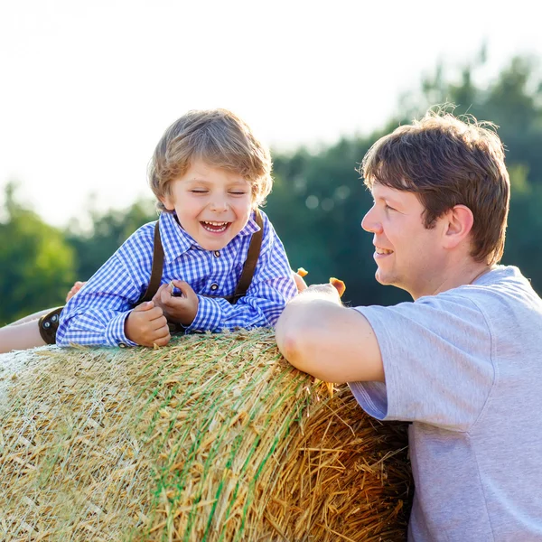Pai e pequeno filho se divertindo no campo de feno amarelo no verão — Fotografia de Stock