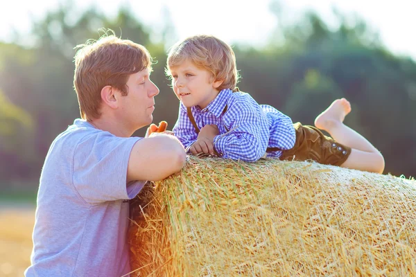 Отец и маленький сын веселятся на желтом сеновале летом — стоковое фото