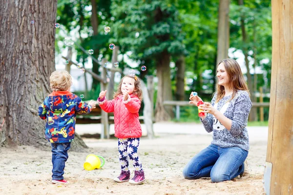 Moeder en twee kleine kinderen spelen op speelplaats — Stockfoto