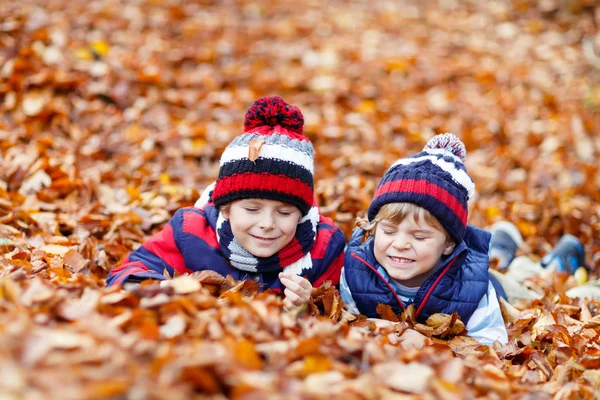Sonbahar yapraklarında, parkta yatan iki küçük çocuk.. — Stok fotoğraf