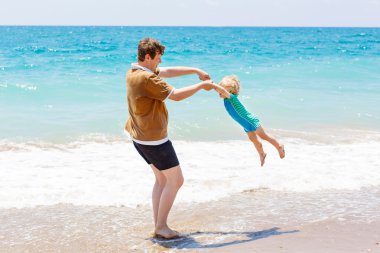Baba ve küçük yürümeye başlayan çocuk kumsalda eğleniyor