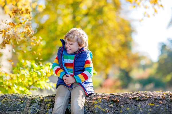 Little blond kid playing with yellow leaves in autumn park. — Stock Photo, Image