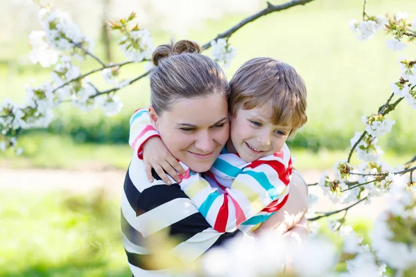 Ung mamma och lilla kid boy roar sig i blommande trädgård — Stockfoto