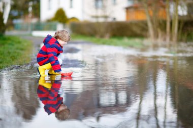 Küçük çocuk çocuk su birikintisi tarafından kağıt tekne ile oynuyor