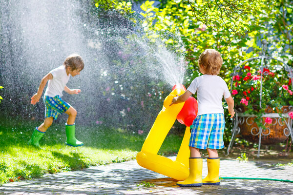 Two little kids playing with garden hose in summer