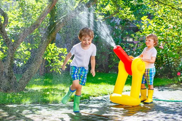 Due bambini piccoli che giocano con tubo da giardino e acqua in estate — Foto Stock