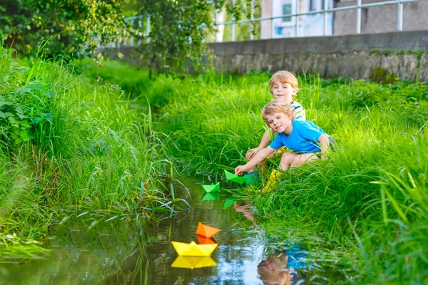 Zwei kleine Brüder spielen mit Papierbooten am Fluss — Stockfoto