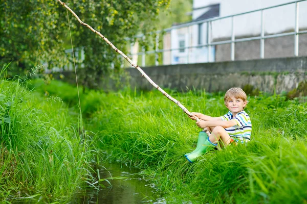 Kleiner Junge angelt mit selbstgebastelter Angelrute auf Fluss — Stockfoto