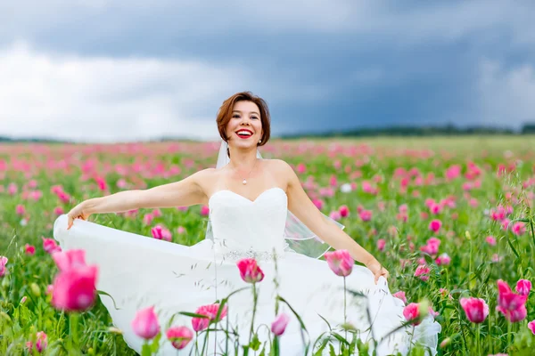 Gelukkige bruid in witte jurk met plezier in bloem klaproos veld — Stockfoto