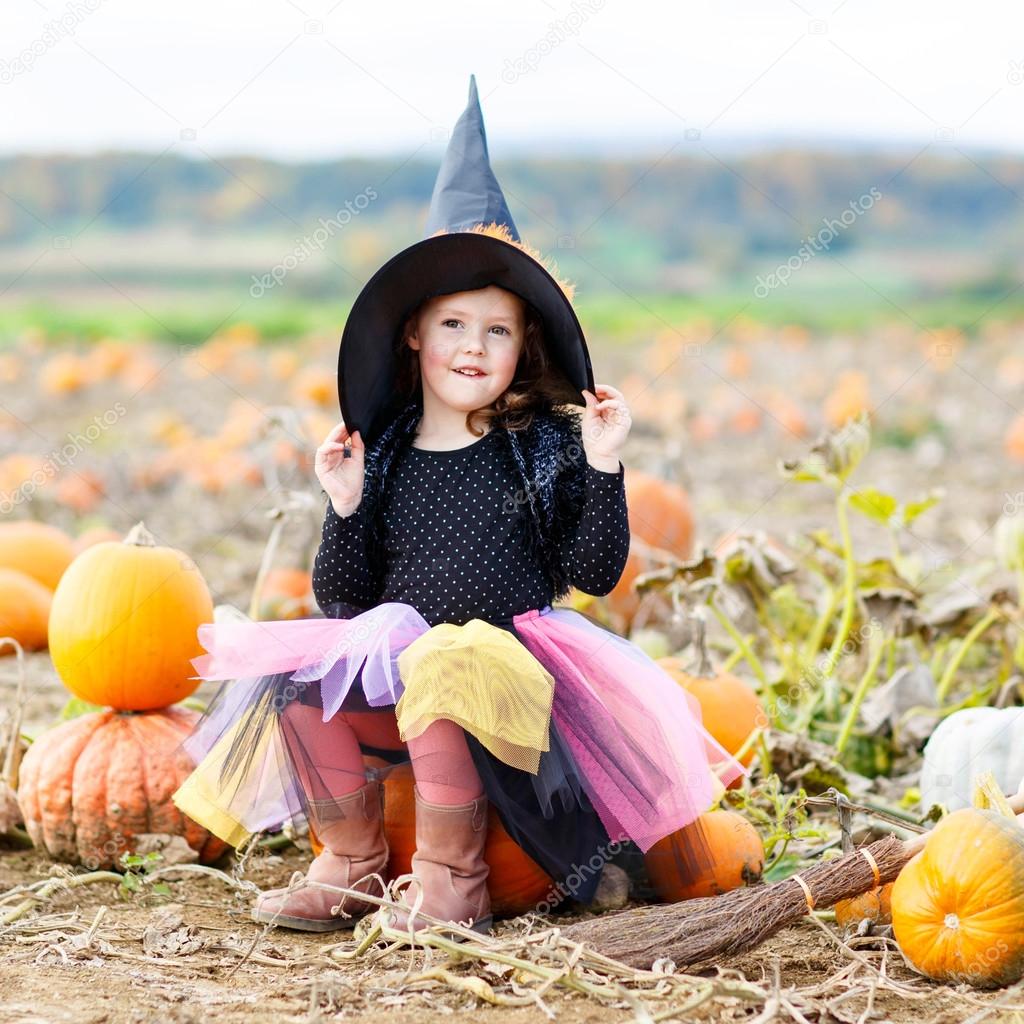 little girl wearing halloween witch costume on pumpkin patch