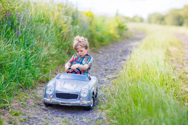 Liten unge pojke köra stor leksaksbil med en björn, utomhus. — Stockfoto