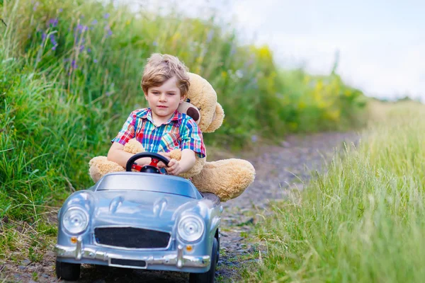 Liten unge pojke köra stor leksaksbil med en björn, utomhus. — Stockfoto