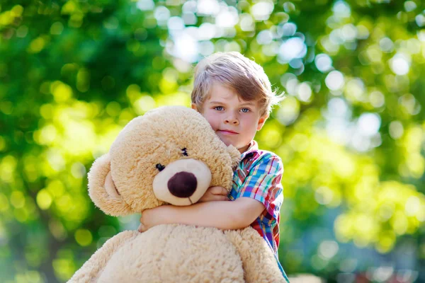 Niño jugando con un gran oso de peluche, al aire libre . — Foto de Stock