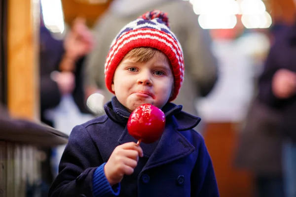 Menino pequeno comendo maçã cristalizada no mercado de Natal — Fotografia de Stock