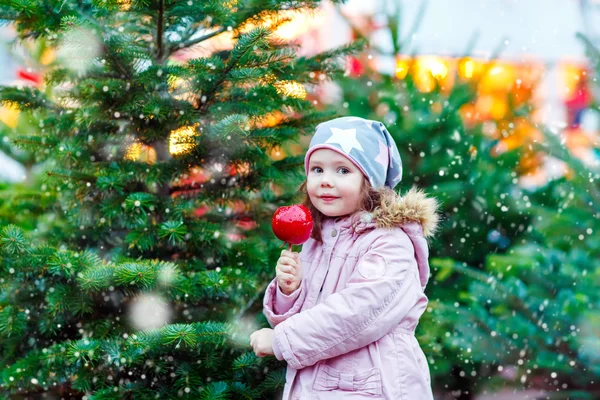 Little kid girl eating crystalized apple on Christmas market — Stock Photo, Image