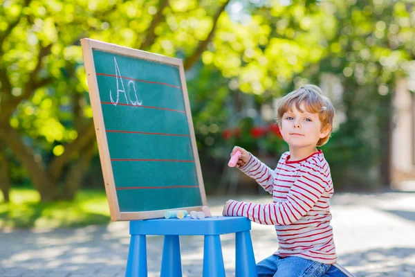 Little boy at blackboard practicing letters — Stock Photo, Image