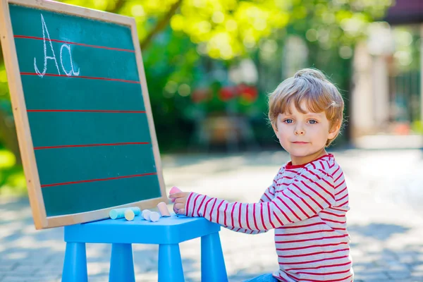Kleiner Junge an der Tafel übt Buchstaben — Stockfoto