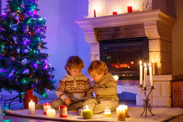 Två små barn sitter vid öppna spisen hemma på jul — Stockfoto