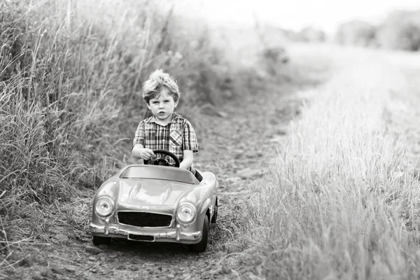 Menino menino dirigindo carro de brinquedo grande com um urso, ao ar livre . — Fotografia de Stock