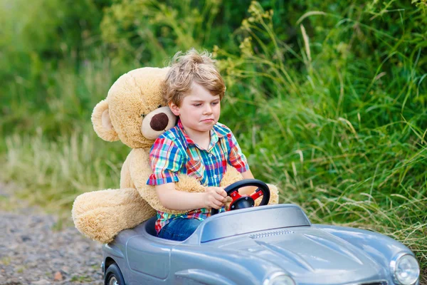 Ragazzino che guida auto giocattolo grande con un orso, all'aperto . — Foto Stock