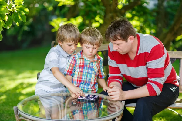 Two little kid boys and father playing together checkers game — Stock Photo, Image