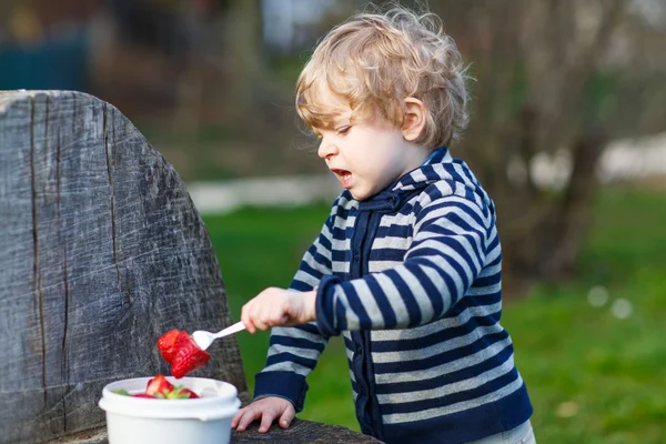 Piękny blond chłopiec dwa lata jeść truskawki na zewnątrz — Zdjęcie stockowe